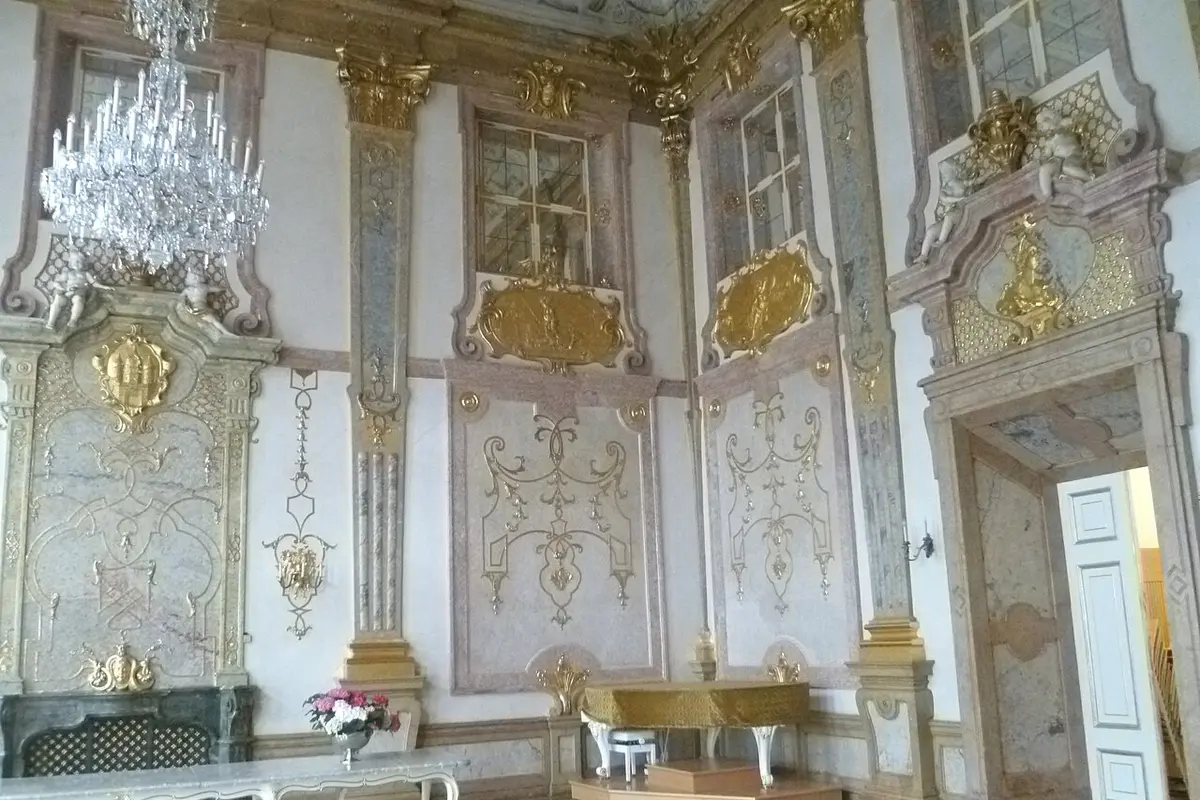 A wall of the Marble Hall with gilded decoration, painted marble panels, a crystal chandelier and a doorway